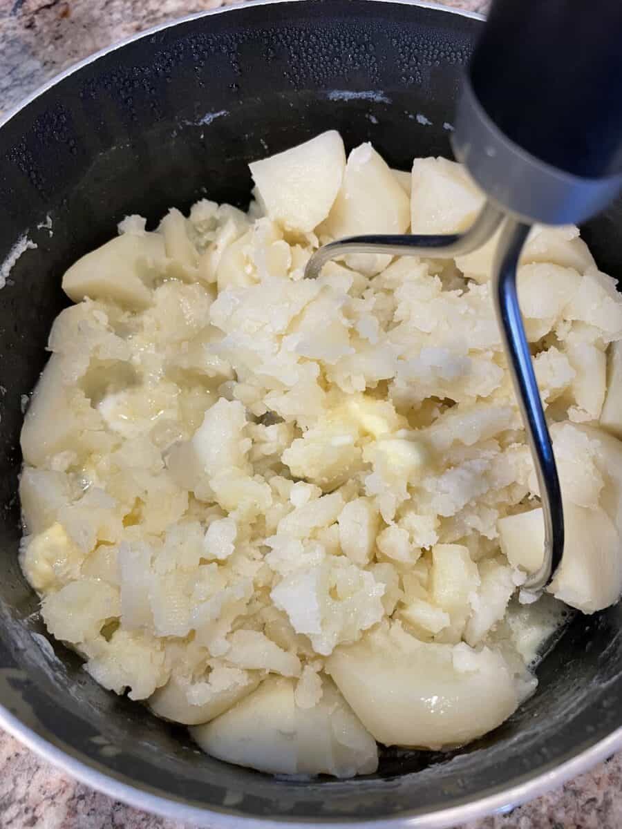 Mashing the Boiled Potatoes with a Handheld Potato Masher.