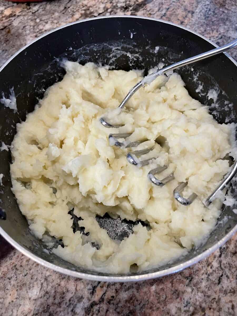 Mashed Potatoes in a Pot Along with a Potato Masher.
