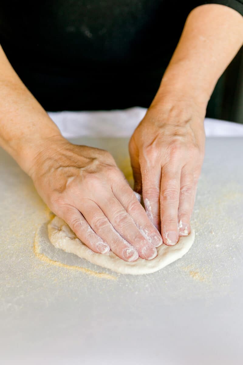 Pressing Out Homemade Pizza Dough on a wooden board with fingertips.  