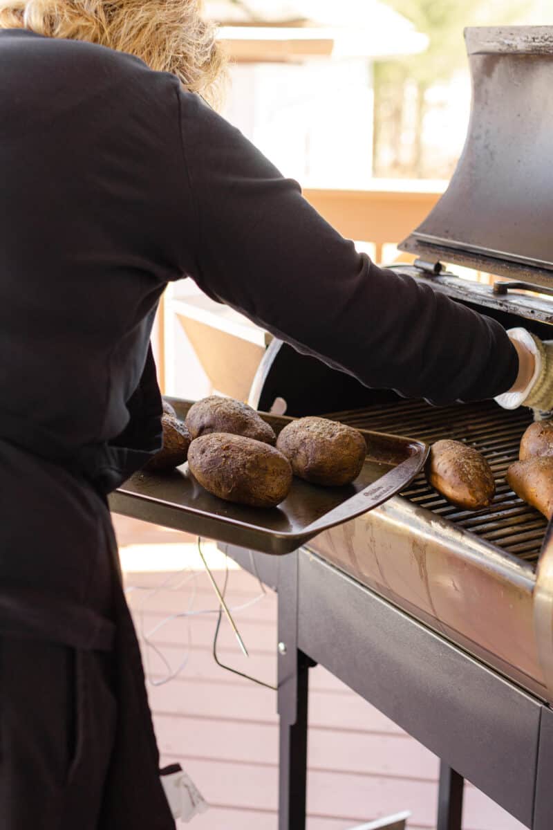 Baked Potatoes on the Smoker Being Removed with Gloved Hands.
