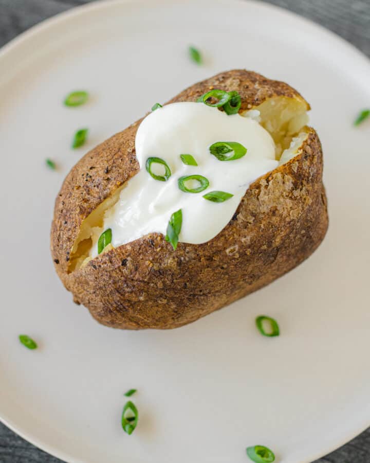 Smoked Baked Potato on a plate topped with a dollop of sour cream and a sprinkling of chives.
