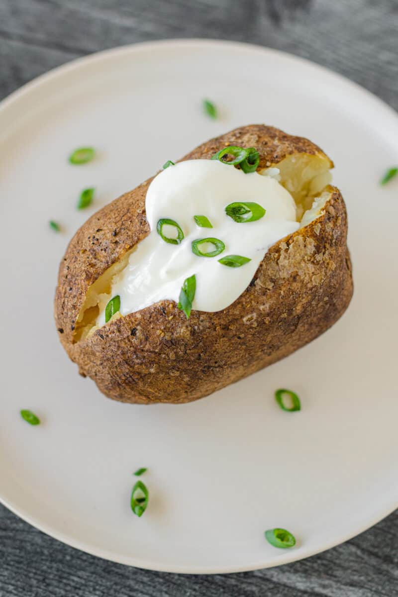 Smoked Baked Potato on a plate topped with a dollop of sour cream and a sprinkling of chives.