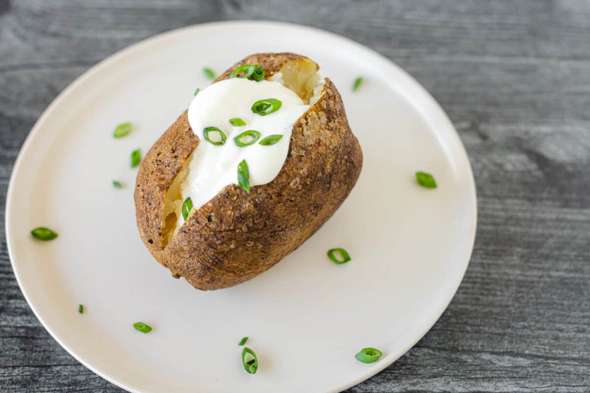 Smoked Baked Potato Recipe on a white plate with sour cream and chives.