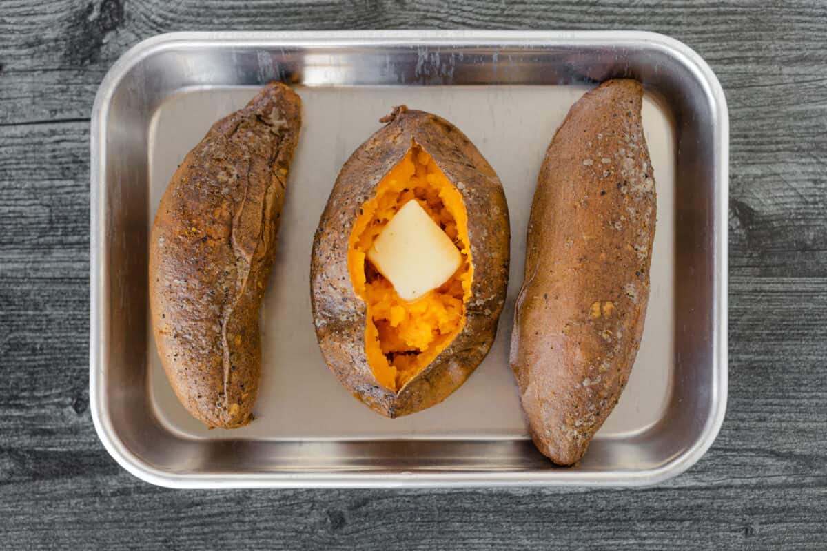 3 Smoked Sweet Potatoes on a tray with the middle one cut open and a pat of butter was placed on top.  