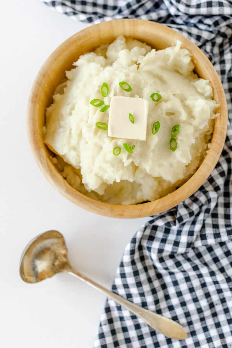 Homemade Mashed Potatoes in a wooden bowl topped with green onion pieces and a pat of butter.