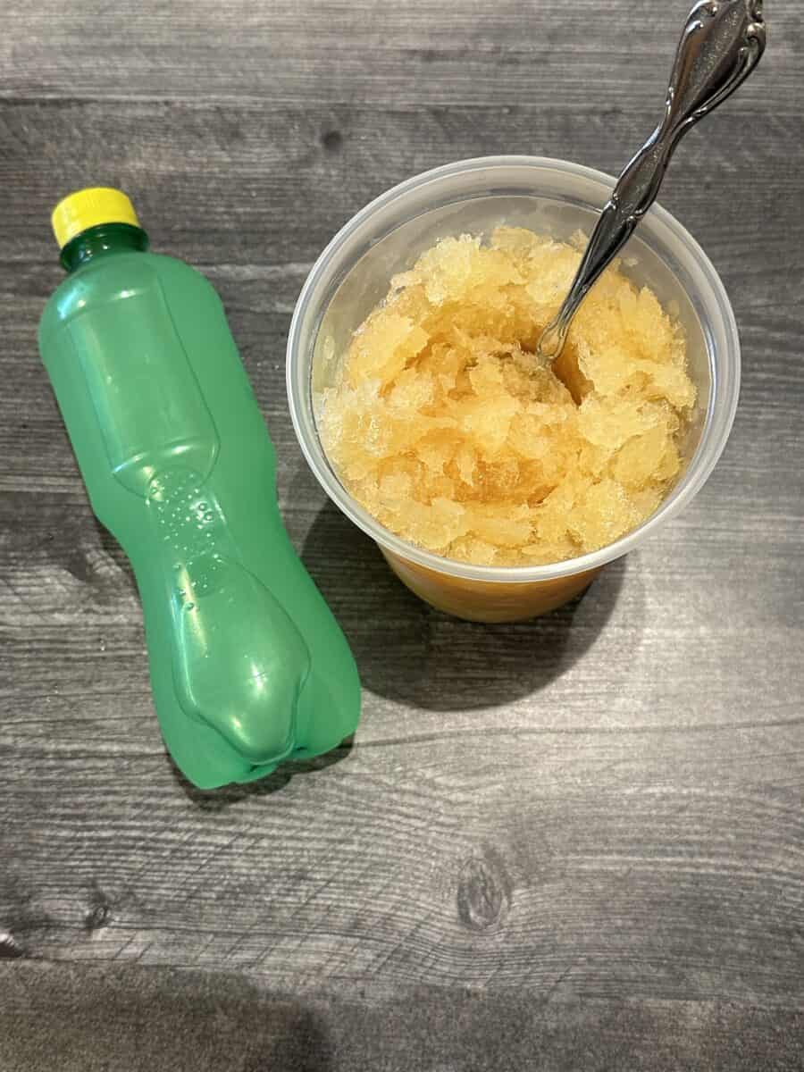Frozen Whiskey Slush in a Container with a Spoon along with a Bottle of Grapefruit Soda.