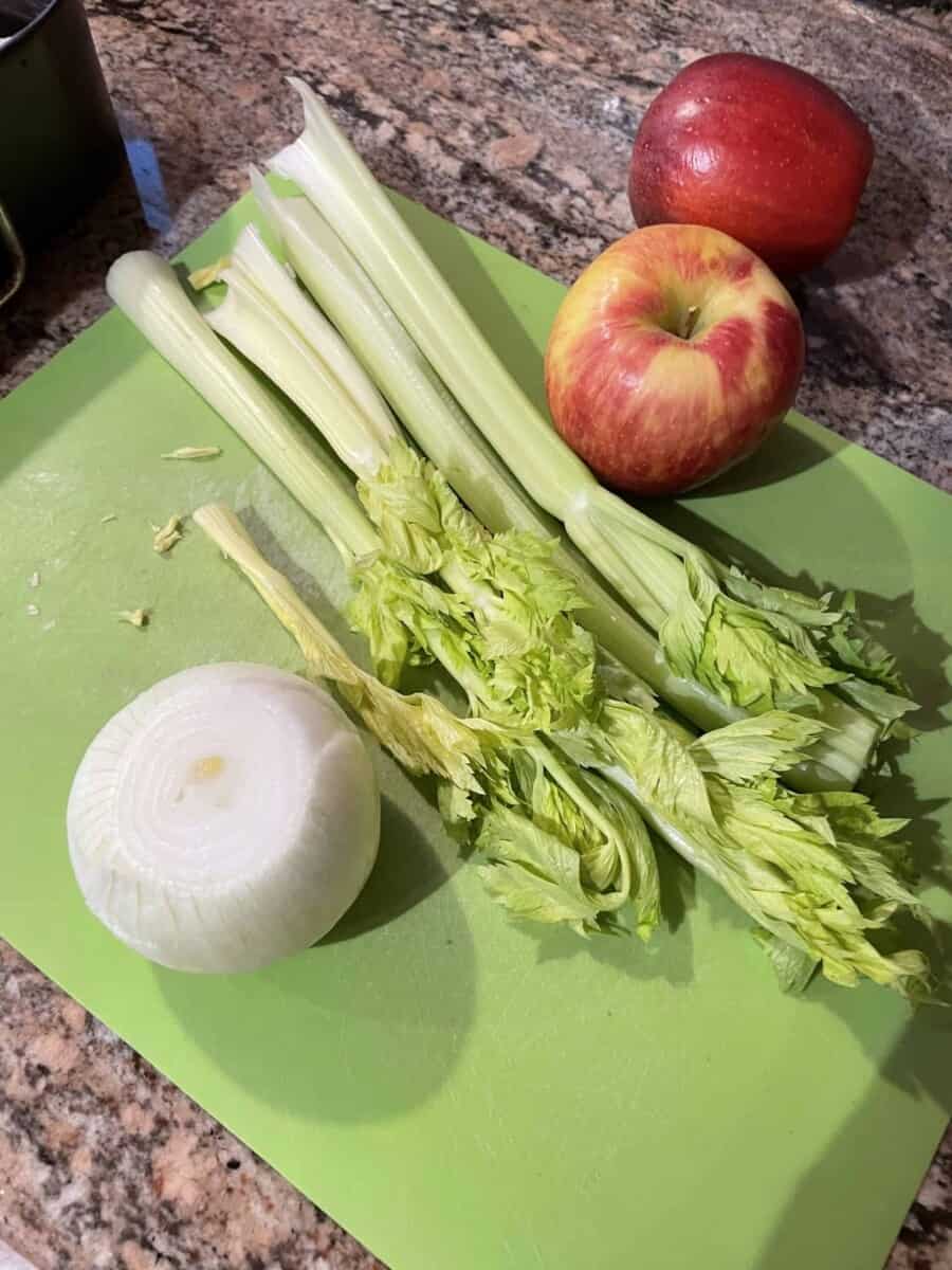 Stalks of Celery, A Whole Onion, and a Few Apples on a Cutting Mat.