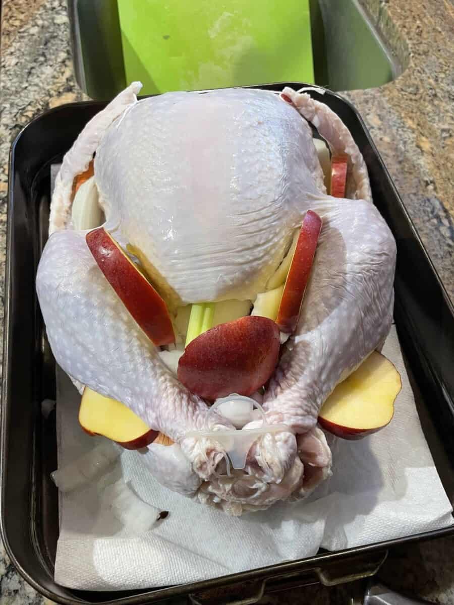 Adding the Celery, Onion, and Apple Pieces to the Brined Turkey and Tying the Turkey Legs Together.