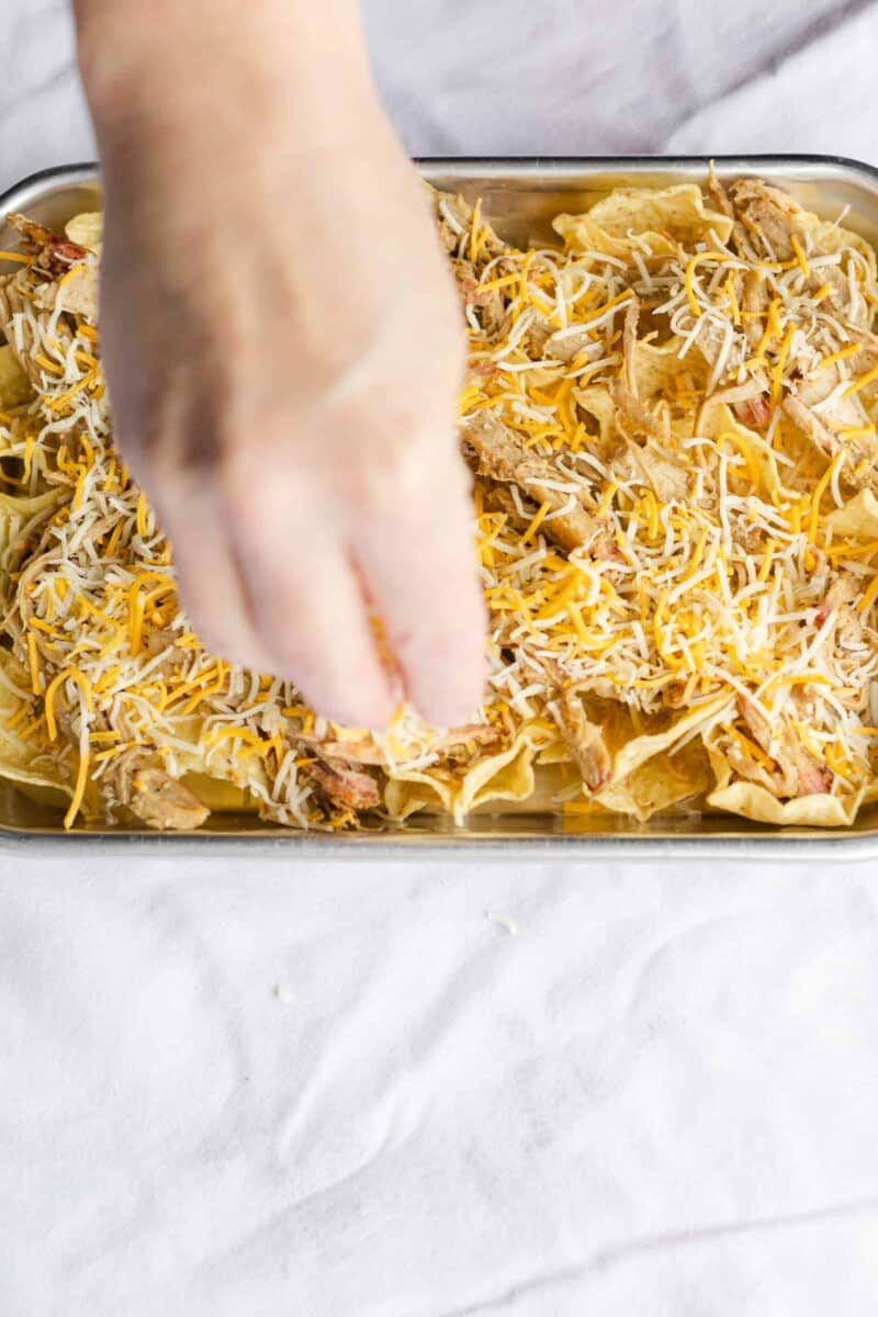Sprinkling Shredded Cheese on top of the Pork and Tortilla Chips.