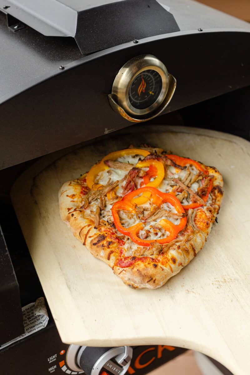 A Pulled Pork Pizza Being Cooked in an Outdoor  Pizza Oven.
