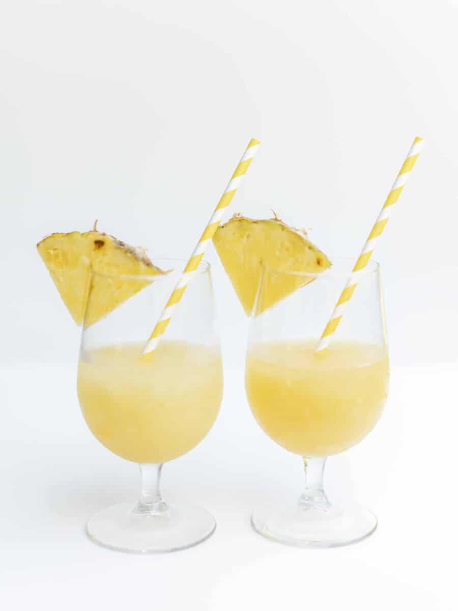 Frozen Pineapple Cocktail in 2 Glasses Garnished with a Pineapple Wedge.