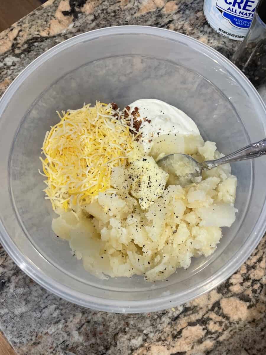 A Bowl with the Baked Potato Inside, Shredded Cheese, Sour Cream, Bacon Bits, Salt, and Pepper