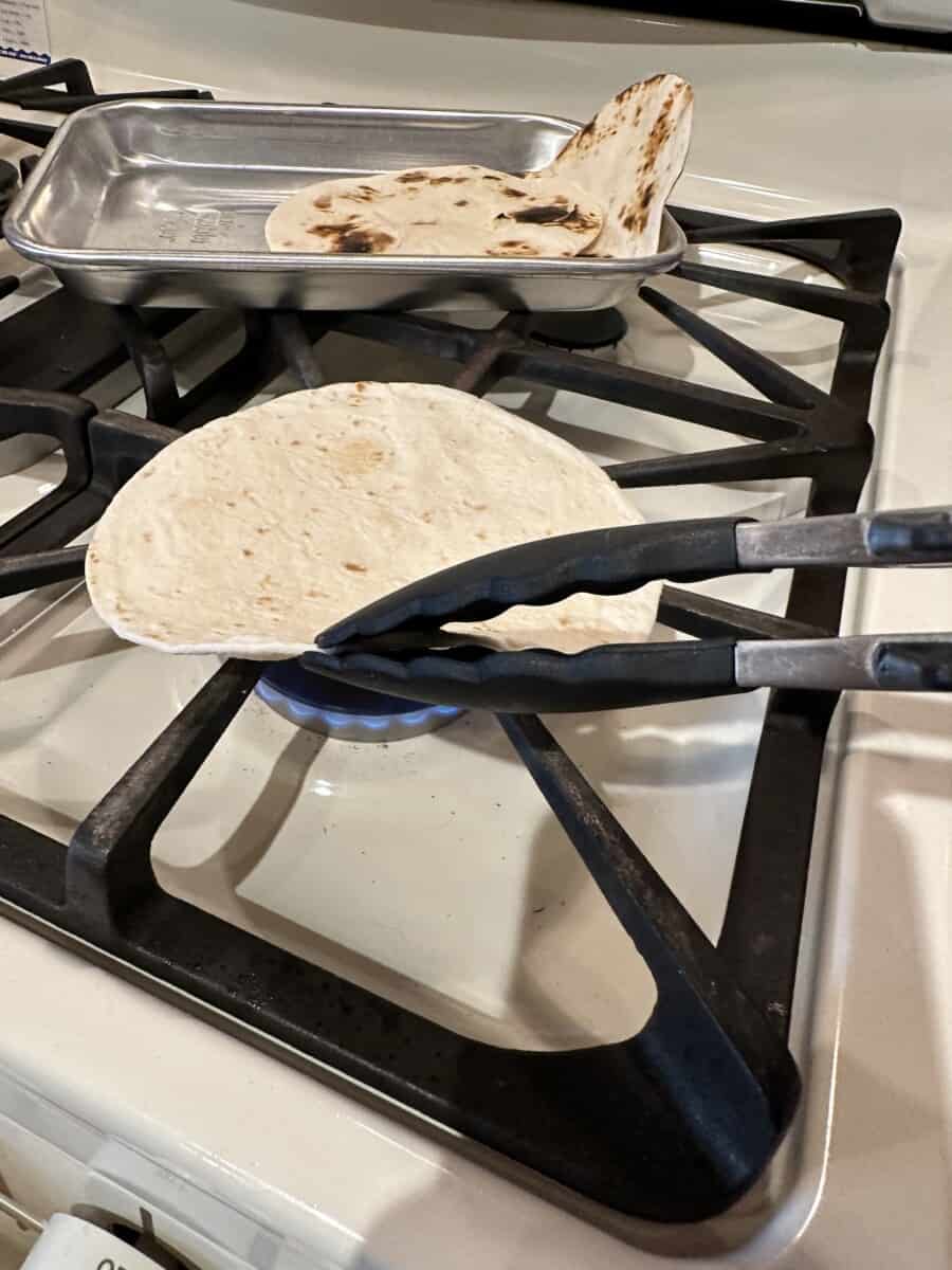 Using a Pair of Tongs to Flip a Soft Tortilla Shell on a Stove Burner.