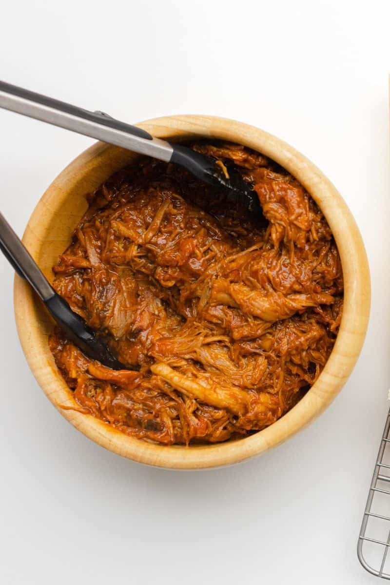 A Bowl of BBQ Pulled Pork along with a pair of tongs.