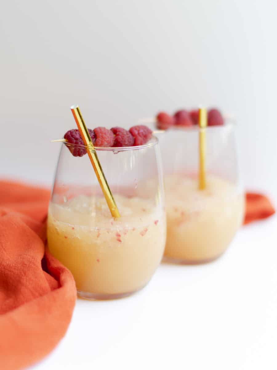 Frozen Raspberry Lemonade Cocktail in a wine glass, with a fresh raspberries garnish and a golden straw.