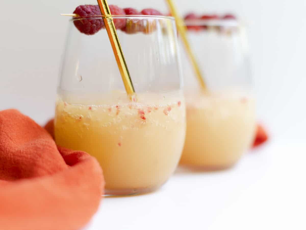 Frozen Raspberry Slush in a wine glass, with a fresh raspberries garnish and a golden straw.