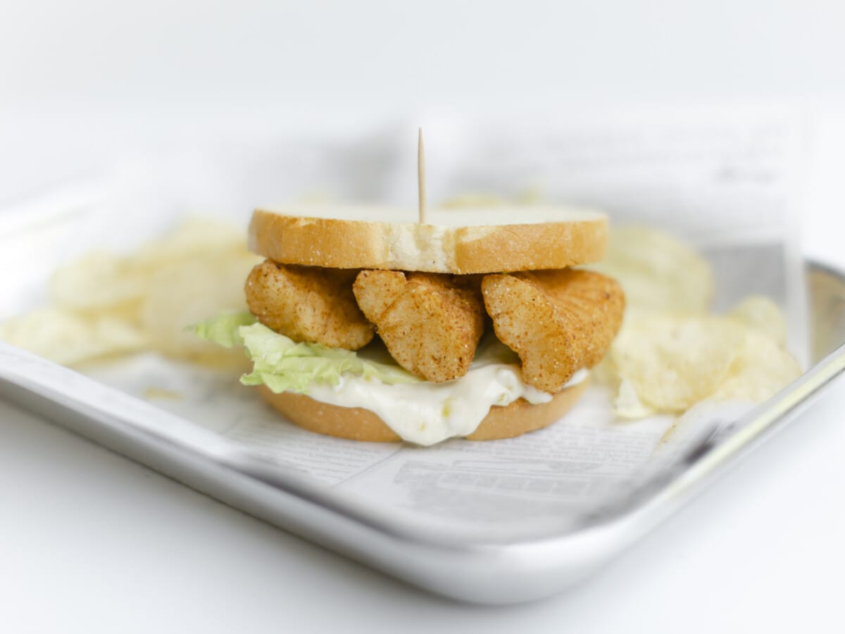 Walleye Sandwich with lettuce and tartar sauce on a serving tray with a side of potato chips.