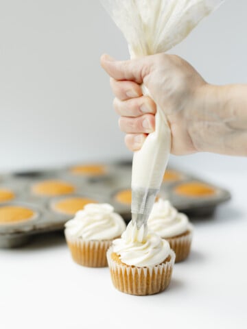 Piping Cream Cheese Frosting onto Pumpkin Cupcakes