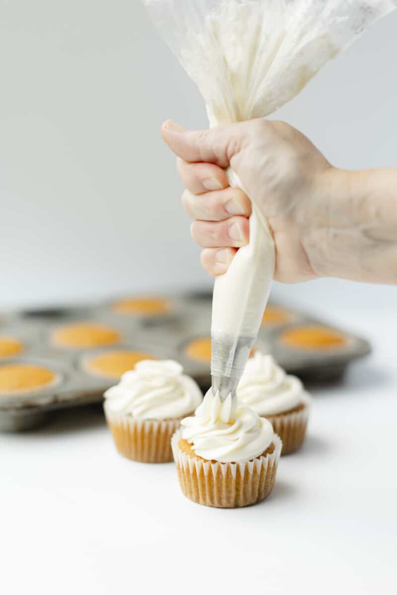 Piping Cream Cheese Frosting onto Pumpkin Cupcakes
