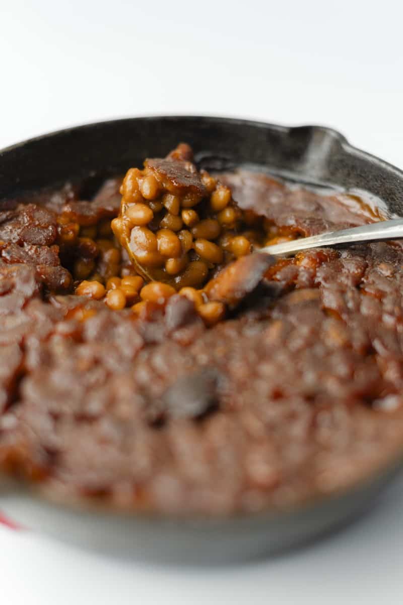 Smoked Baked Beans Recipe in a cast iron skillet with a serving spoon