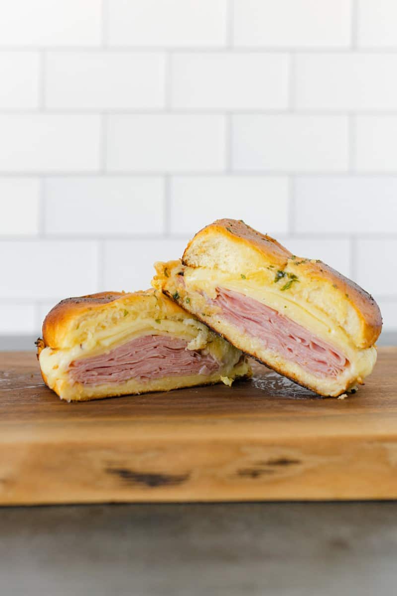 Ham and Cheese Sliders stacked on a wooden borad.
