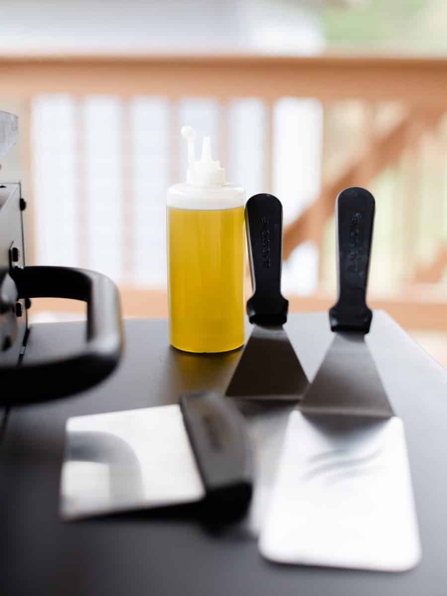 A Pair of Metal Spatulas along with a Griddle Scraper and a Squeeze Bottle of Oil.