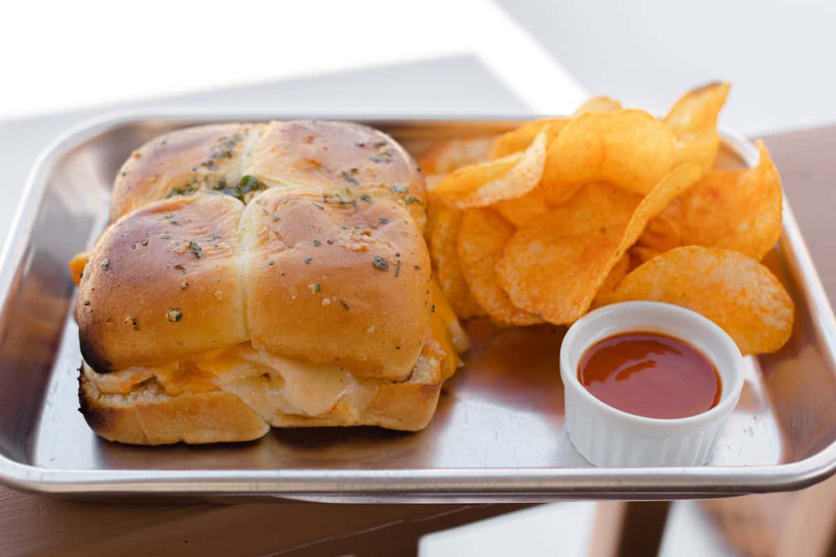 Chicken Sliders on a serving tray with Potato Chips and a side of buffalo sauce.