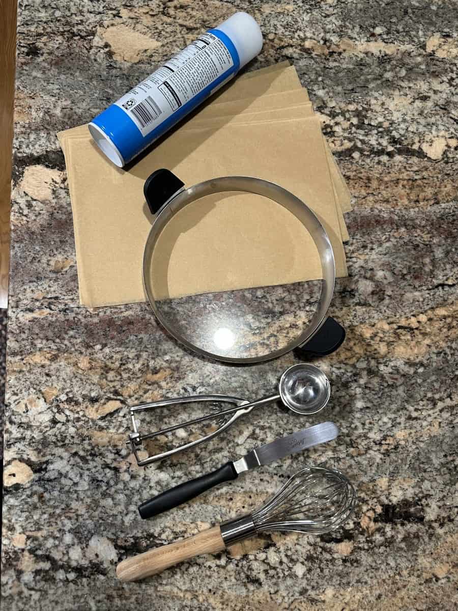 Supplies for Boston Cream Pie: parchment paper, cooking spray, omelette ring, portion scooper, and offset spatula.